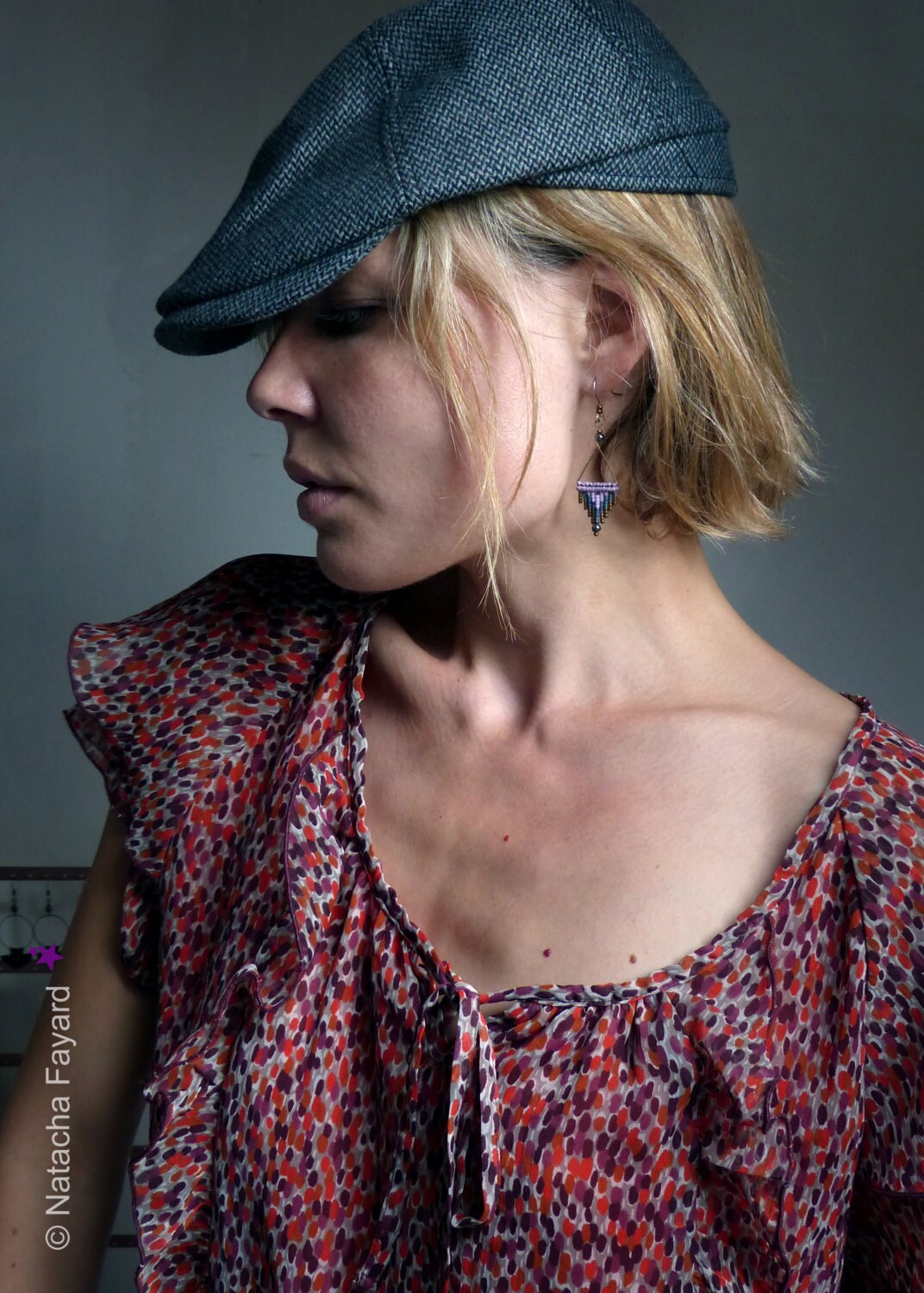 Peut inclure: Une femme portant une casquette plate grise et un chemisier à motifs rouge et blanc avec une boucle d'oreille pendante triangulaire.