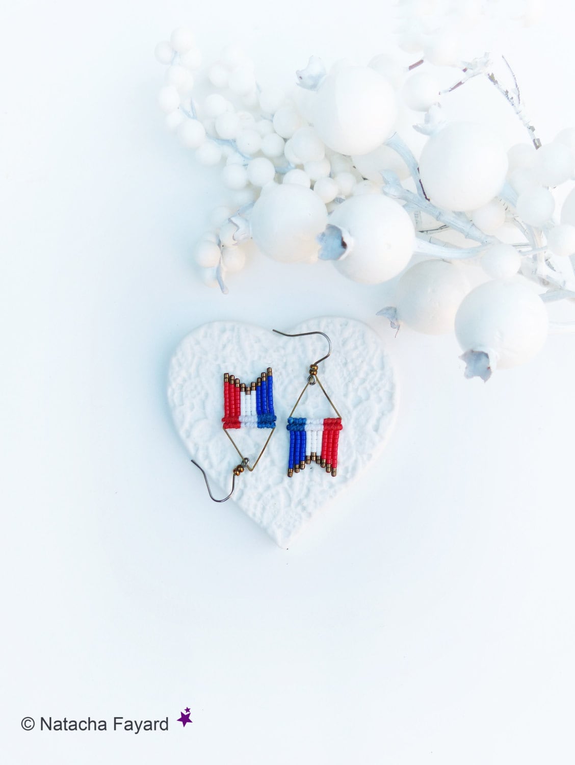 Peut inclure: Une paire de boucles d'oreilles en perles avec un motif de drapeau français. Les boucles d'oreilles sont suspendues à un plat en forme de cœur blanc.