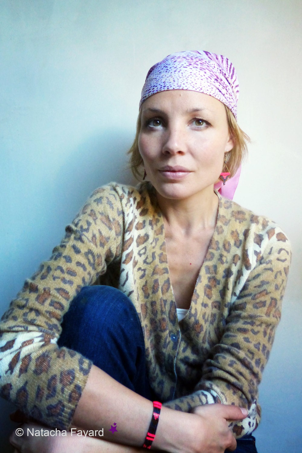 Peut inclure: Une femme portant un cardigan à imprimé léopard avec un foulard à motifs roses et violets. Elle porte un jean bleu et un bracelet au poignet.