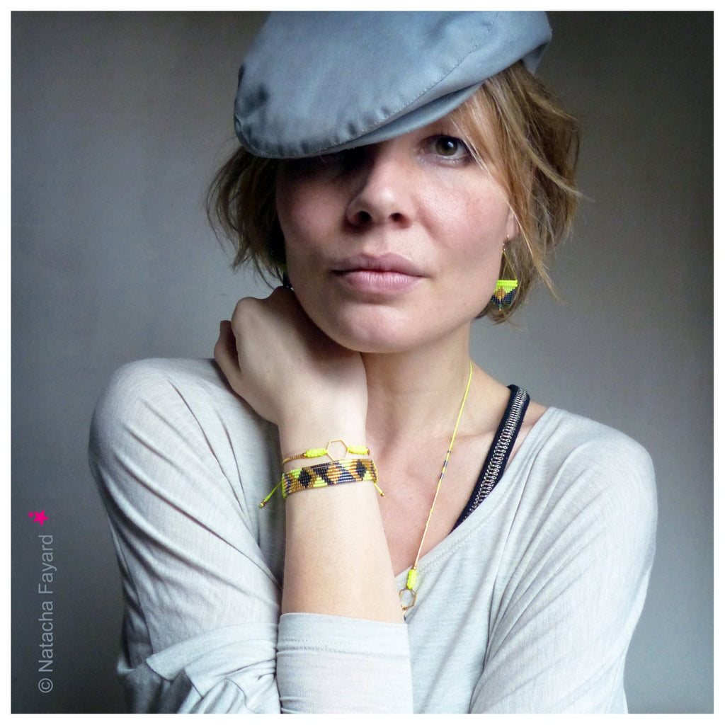 Peut inclure: Une femme portant une casquette plate grise, une chemise rayée gris et blanc et un bracelet en perles jaunes et noires. Elle porte également un collier et des boucles d'oreilles en or.