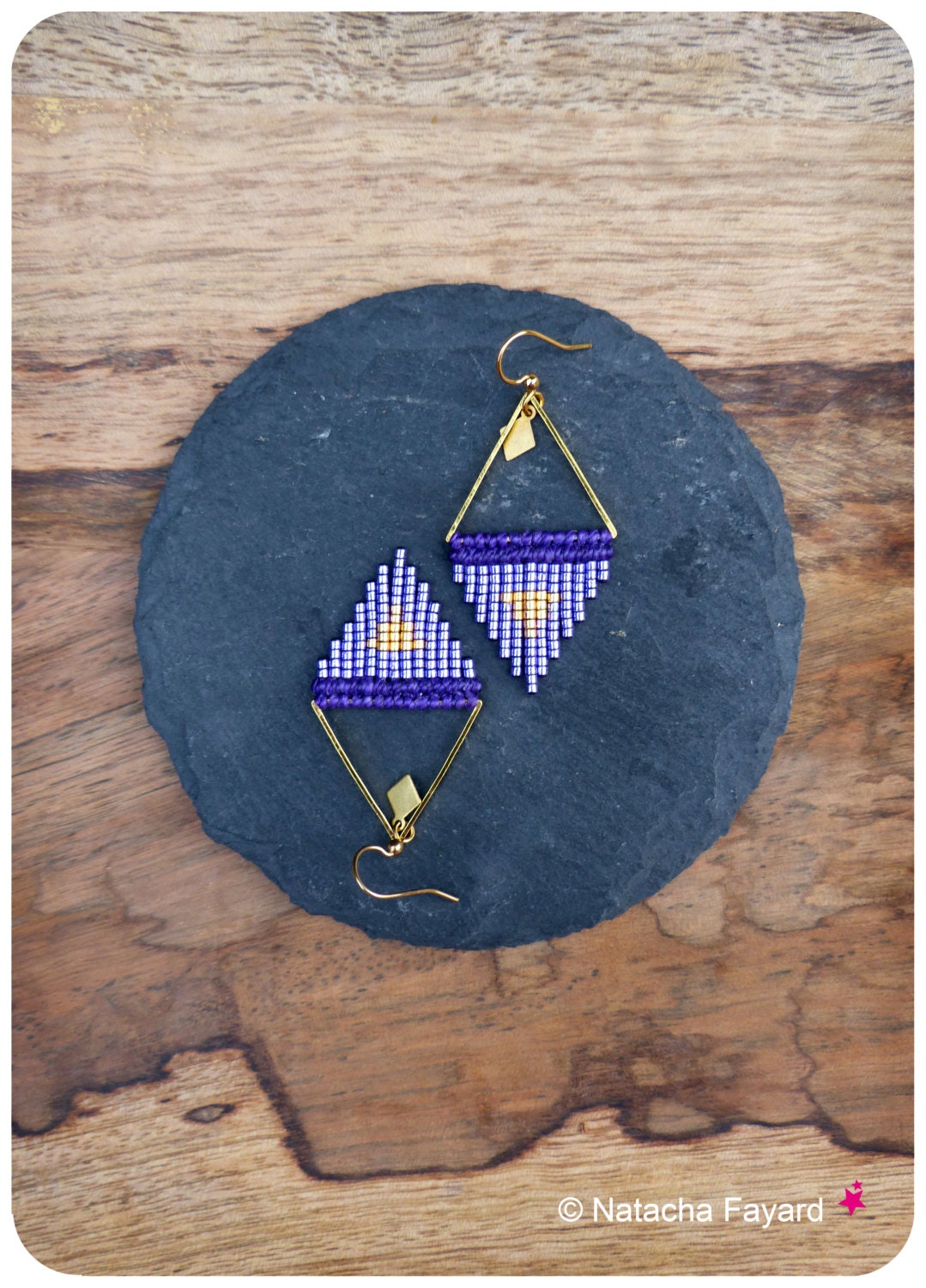 Peut inclure: Paire de boucles d'oreilles faites à la main avec un motif géométrique. Elles présentent un cadre en métal doré en forme de losange, rempli de petites perles violettes, blanches et dorées. Elles sont présentées sur une pierre sombre. Accessoire élégant.