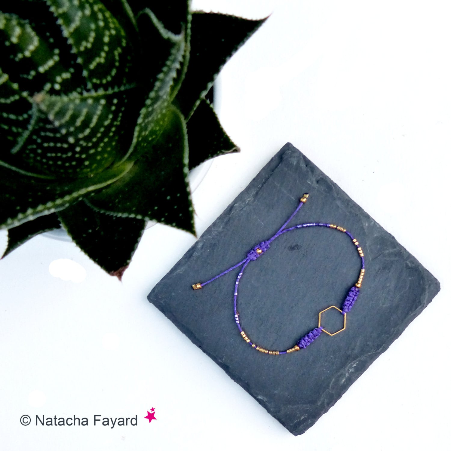 Peut inclure: Un bracelet en cordon violet doté d'une breloque hexagonale dorée centrale, agrémenté de petites perles dorées et de nœuds en macramé violets. Le bracelet comprend une fermeture coulissante réglable avec des perles dorées aux extrémités.