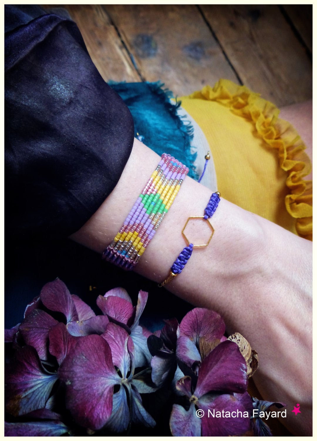 Peut inclure: Un large bracelet en perles tissées avec un motif géométrique en lavande, jaune, rose et vert, accompagné d'un bracelet en cordon violet centré d'une breloque hexagonale dorée. Le texte "© Natacha Fayard" est visible sur l'image.