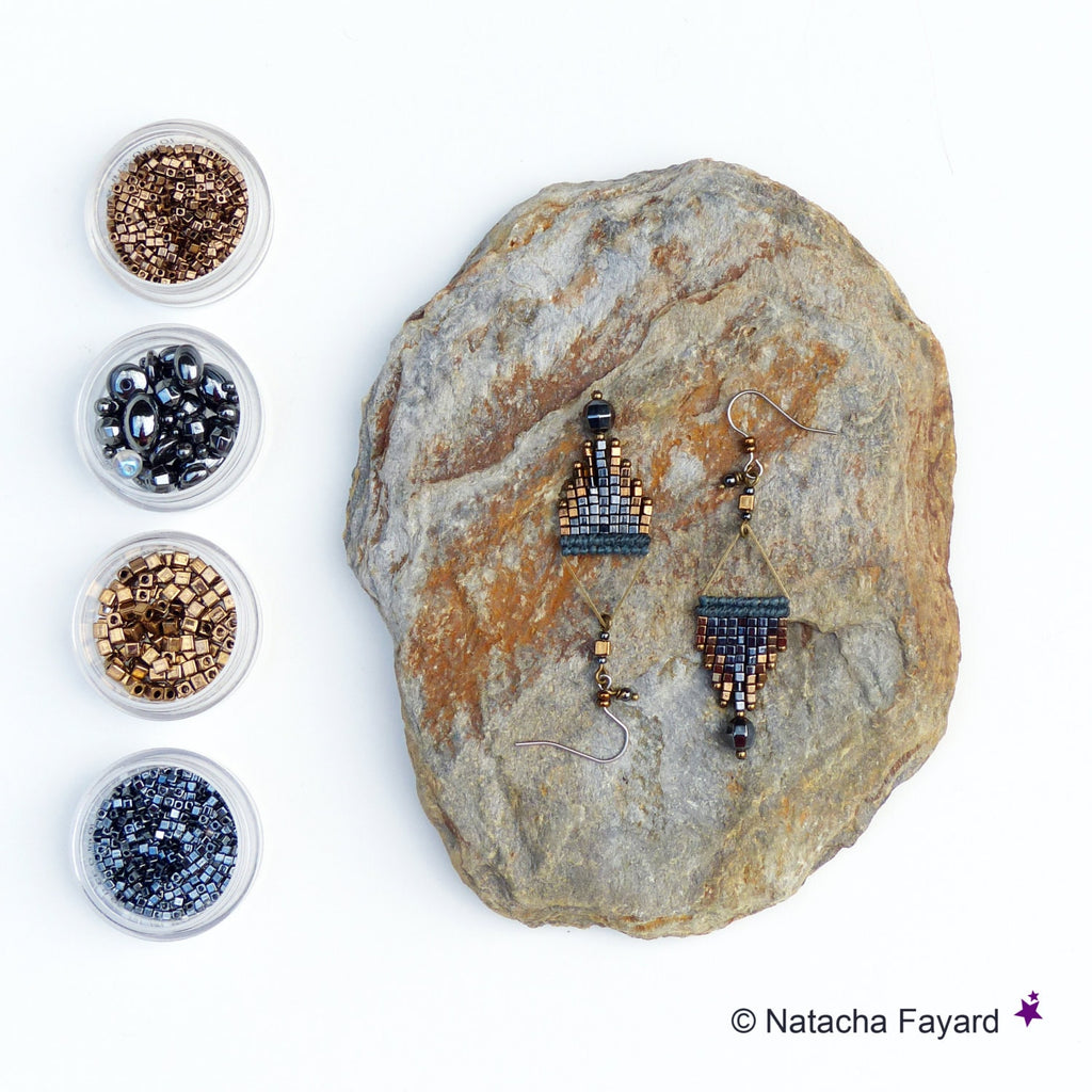 Peut inclure: Une paire de boucles d'oreilles pendantes avec des motifs géométriques en perles noires, brunes et dorées. Les boucles d'oreilles sont présentées sur un rocher avec de petits contenants de perles en arrière-plan.