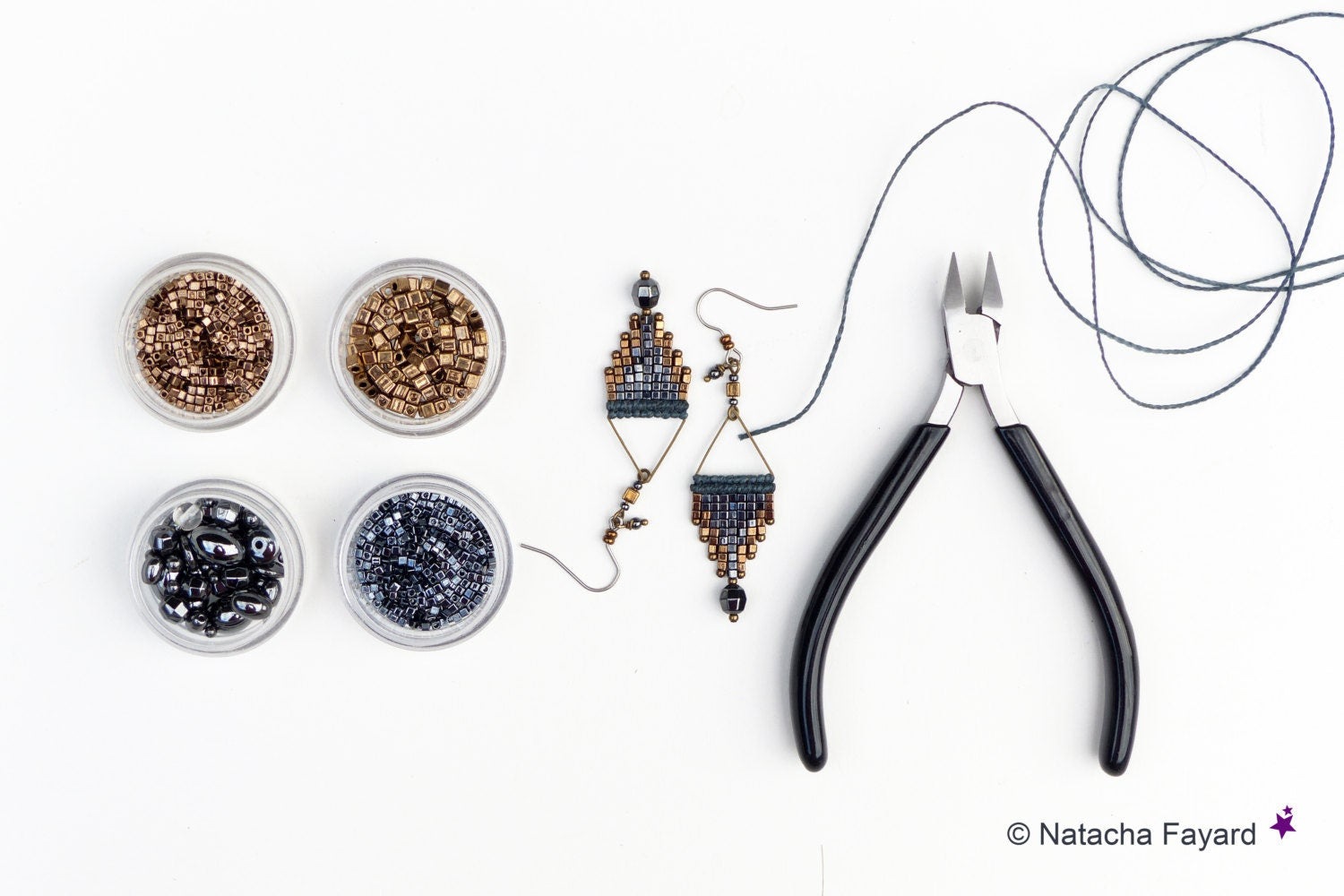Peut inclure: Deux paires de boucles d'oreilles en perles avec un motif géométrique dans des tons de bleu, noir et or. Les boucles d'oreilles sont présentées sur une surface blanche avec de petits contenants de perles, une bobine de fil et des pinces coupantes.