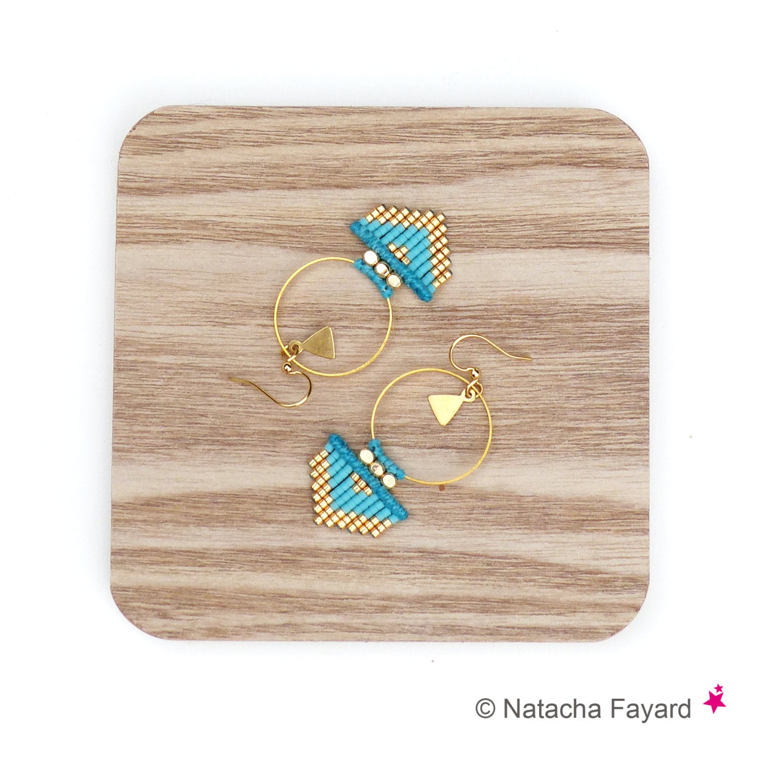 Peut inclure: Une paire de boucles d'oreilles créoles dorées avec des franges de perles turquoise et dorées qui pendent du bas. Les boucles d'oreilles sont sur une surface en bois.