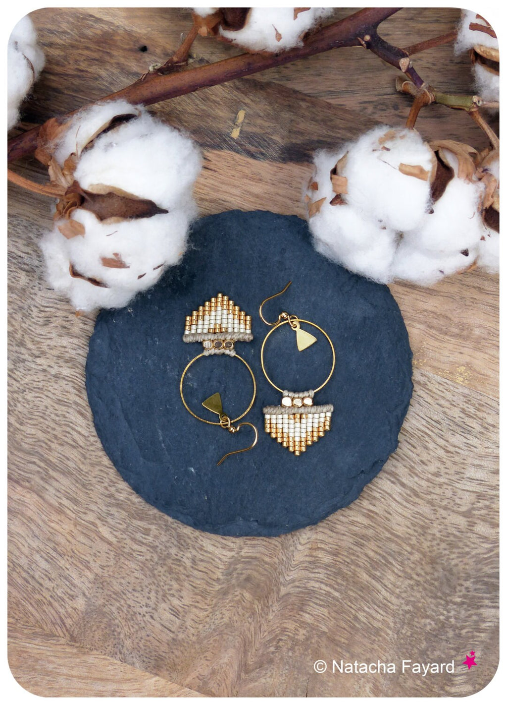Peut inclure: Une paire de boucles d'oreilles créoles dorées avec un motif géométrique composé de perles blanches et dorées. Les boucles d'oreilles sont sur une surface en ardoise noire.