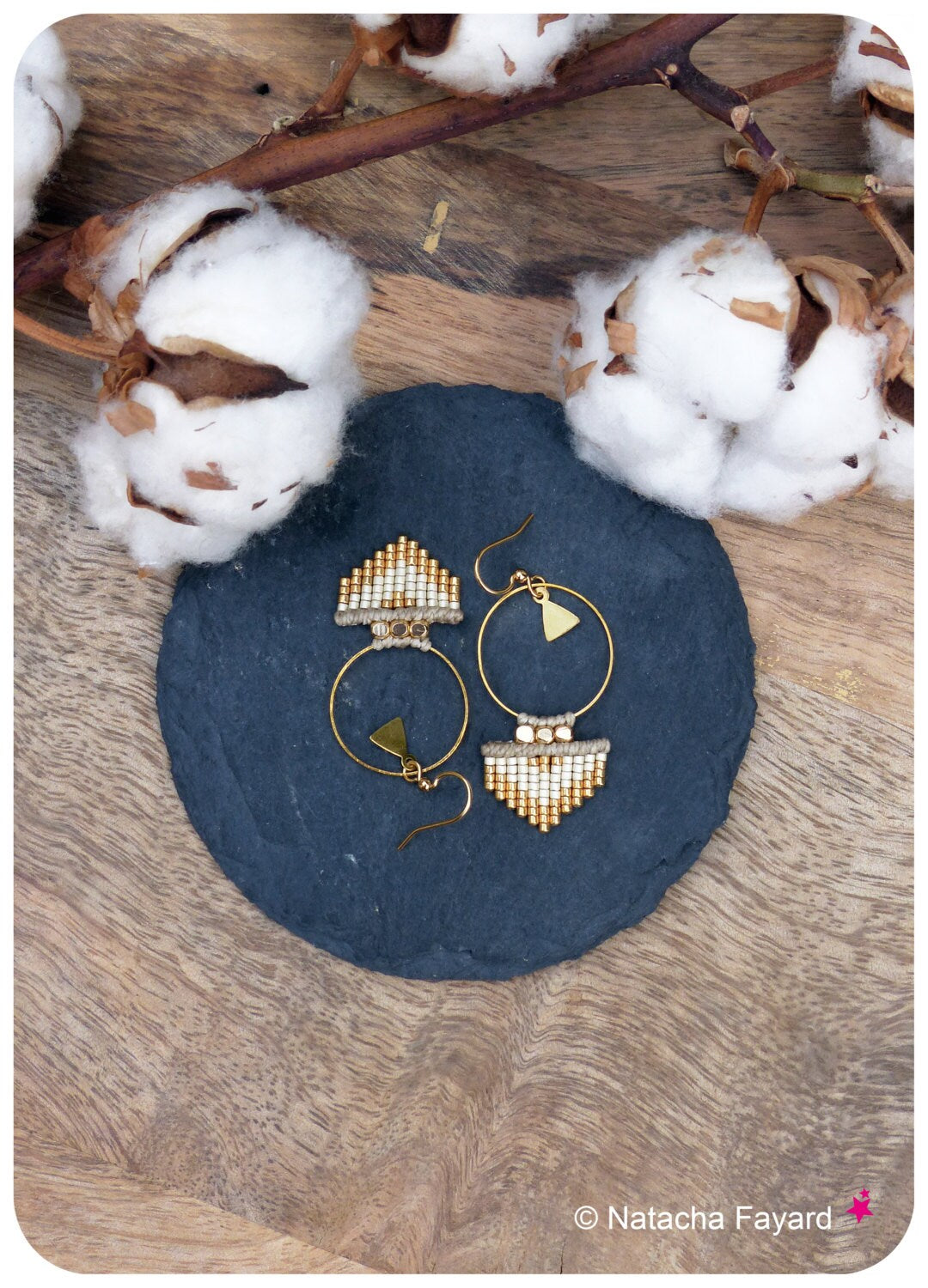 Peut inclure: Une paire de boucles d'oreilles créoles dorées avec un motif géométrique composé de perles blanches et dorées. Les boucles d'oreilles sont sur une surface en ardoise noire.