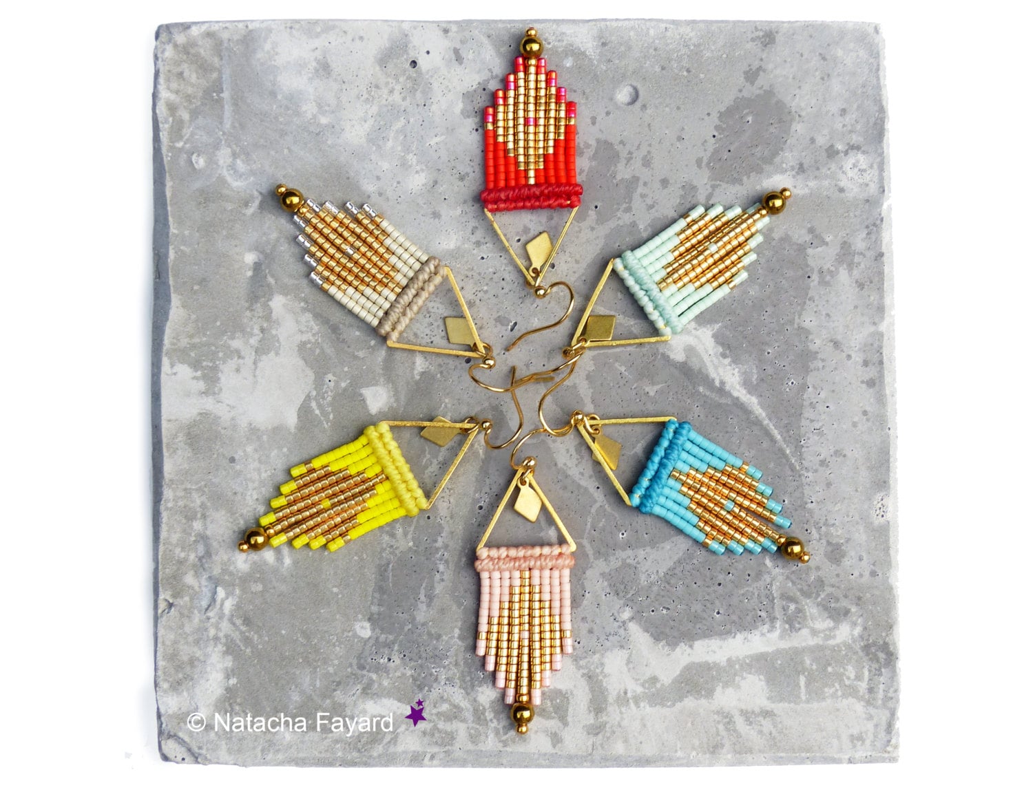 Peut inclure: Une collection de boucles d'oreilles perlées faites à la main, de différentes couleurs, dont le rouge, le jaune, le bleu et le rose. Chaque boucle d'oreille présente un cadre triangulaire doré et une frange de perles. Les boucles d'oreilles sont disposées sur une surface grise.