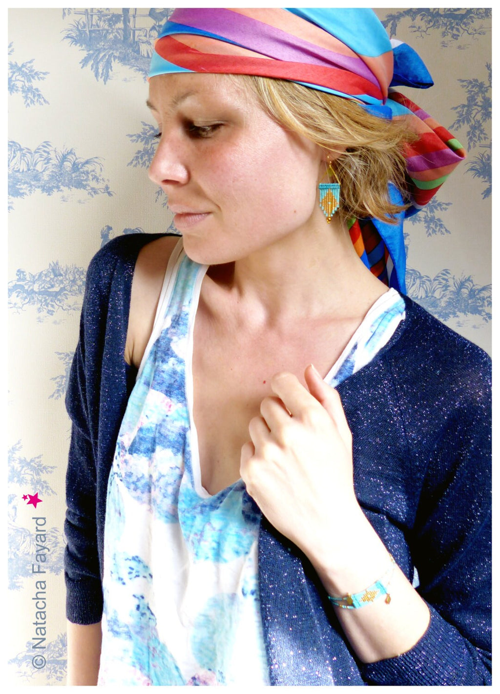 Peut inclure: Une femme portant un foulard rayé bleu et rouge, un haut blanc à motif bleu et rose et un cardigan bleu foncé. Elle porte une paire de boucles d'oreilles turquoise et or et un bracelet turquoise et or.