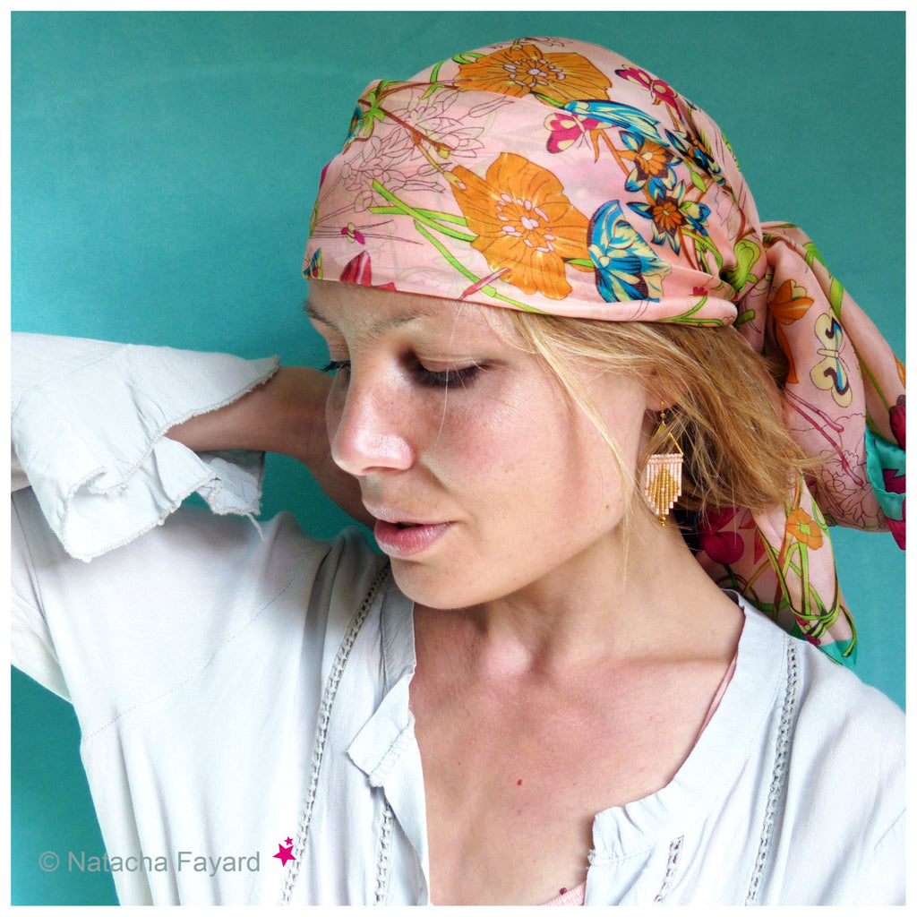 Peut inclure: Une femme aux cheveux blonds porte une chemise blanche et un foulard floral rose. Elle porte des boucles d'oreilles en perles dorées et roses.