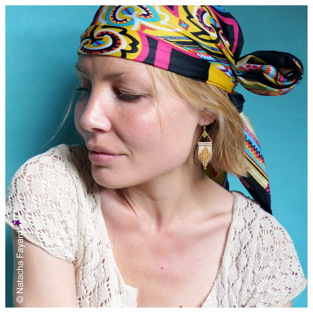 Peut inclure: Une femme portant un foulard à motifs colorés et des boucles d'oreilles en or. Les boucles d'oreilles sont longues et pendantes, avec un design géométrique.